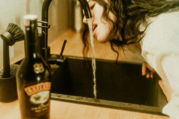 a woman drinking water from a kitchen sink