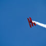 a red plane flying in the sky leaving a trail of smoke behind it