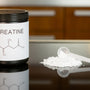 a bottle of creatine next to a spoon on a table