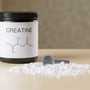 a bottle of creatine next to a spoon on a table